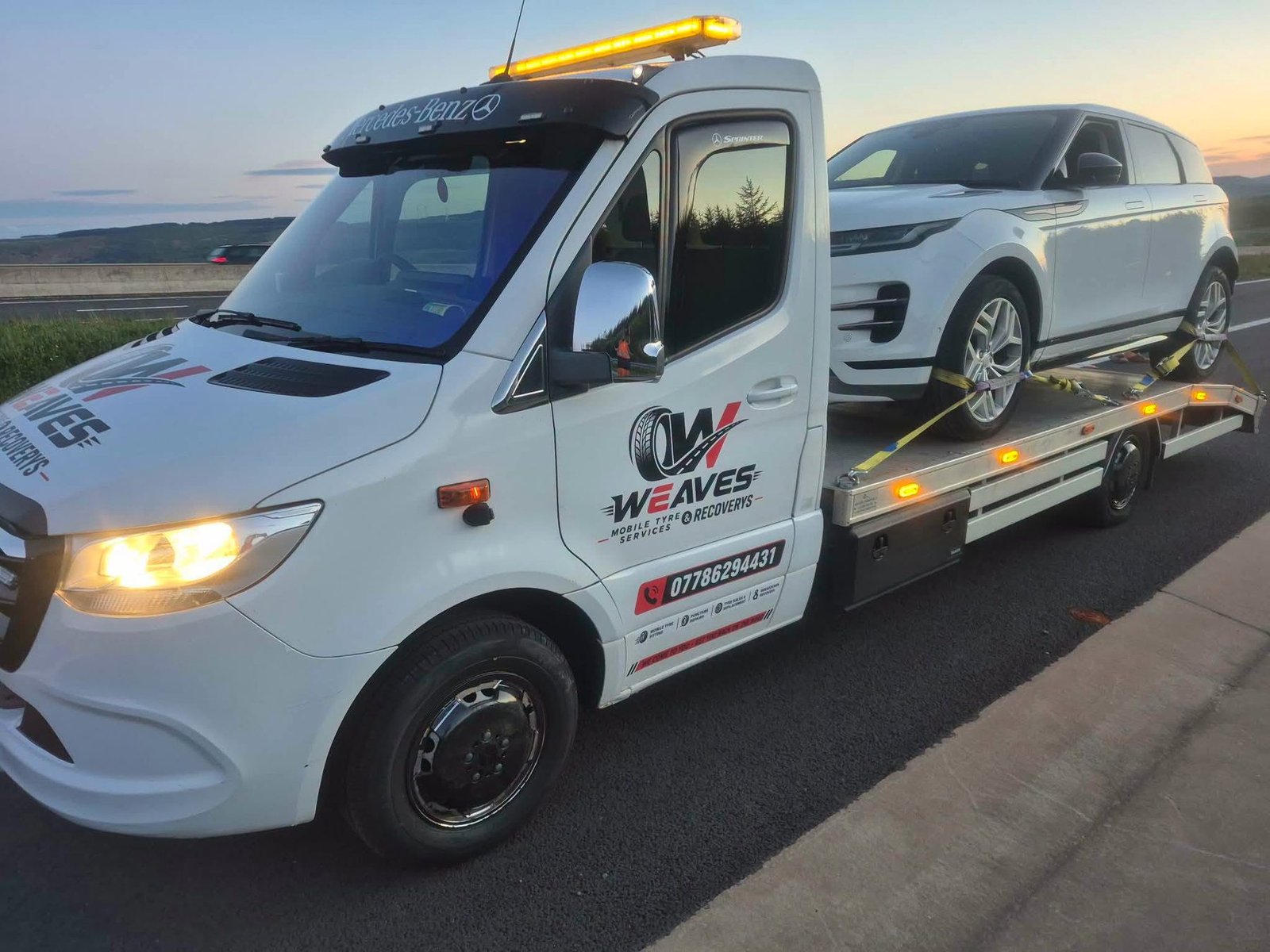 Weaves flatbed recovery truck carrying a Range Rover on a South Wales road at sunset